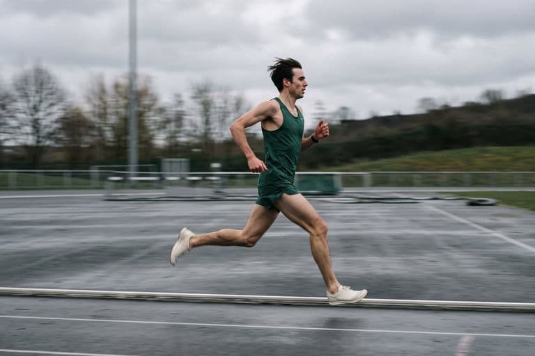 A runner at speed on an outdoor athletics track in flat overcast light