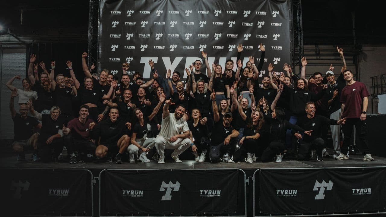 A large group of TYRUN athletes and crew gathered together in front of the event backdrop