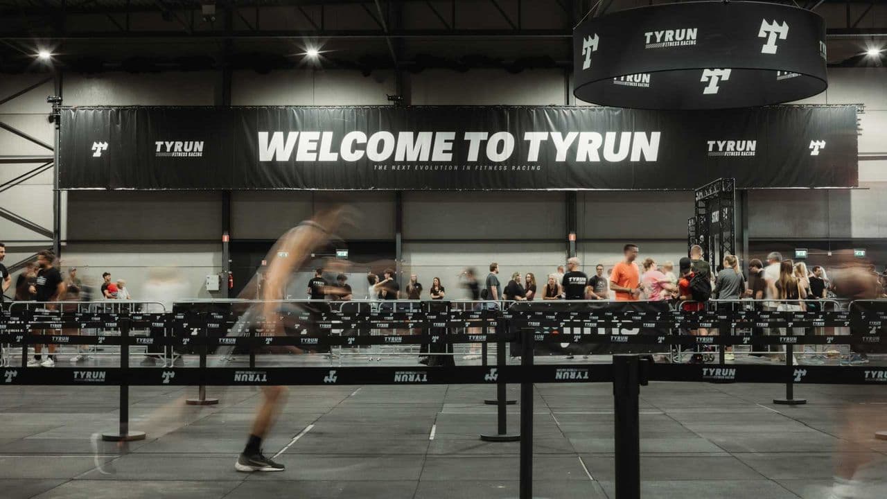 A TYRUN arena floor under a Welcome to TYRUN banner, an athlete running between stations